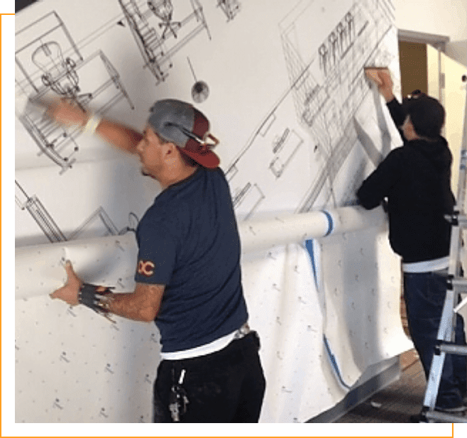 Two men working on a wall with some drawings